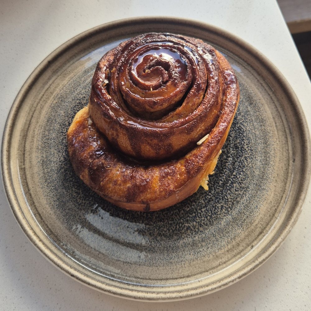 A large glazed cinnamon bun on a stoneware plate at Fika