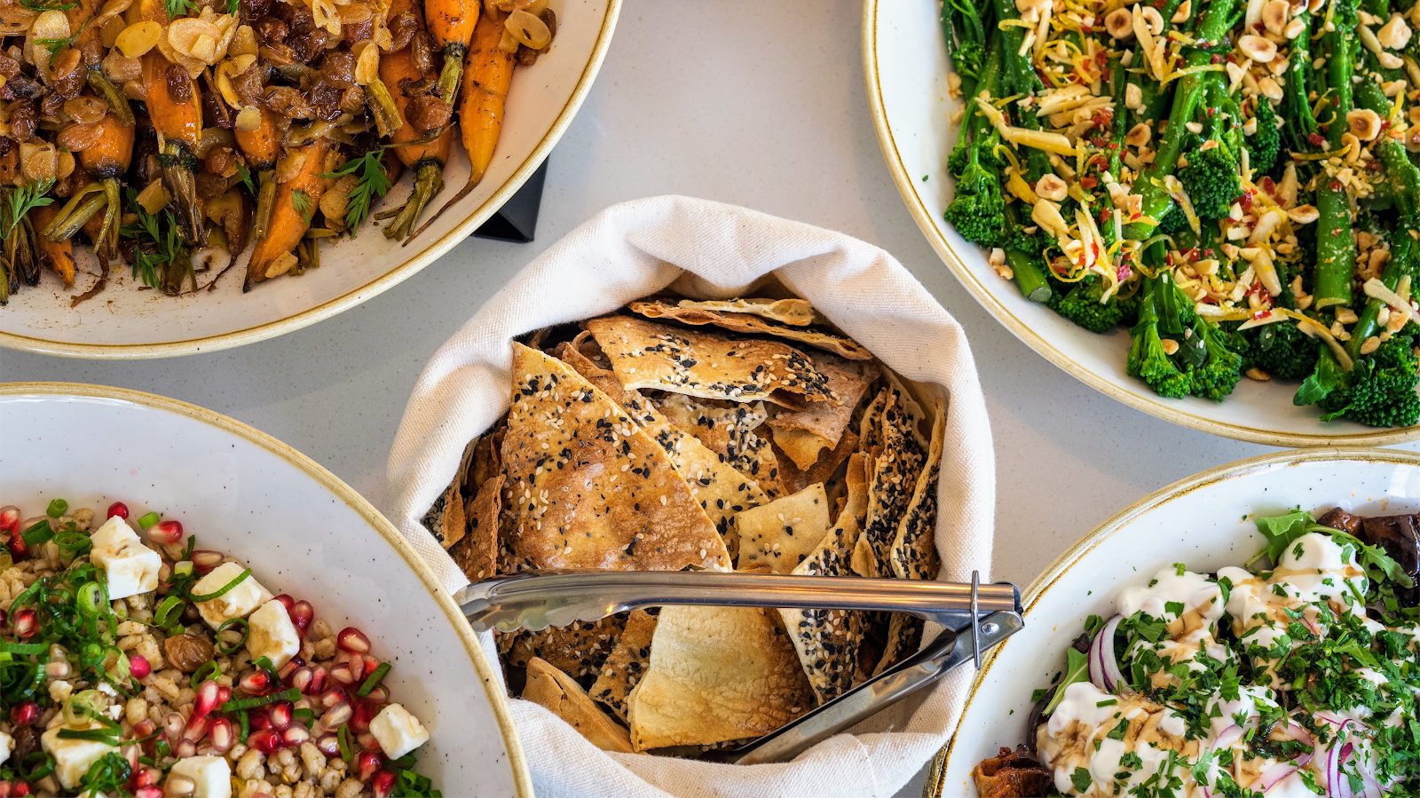 A spread of Fika's deli salads: roasted carrots, tenderstem broccoli and hazelnuts, grain salad and seeded crackers
