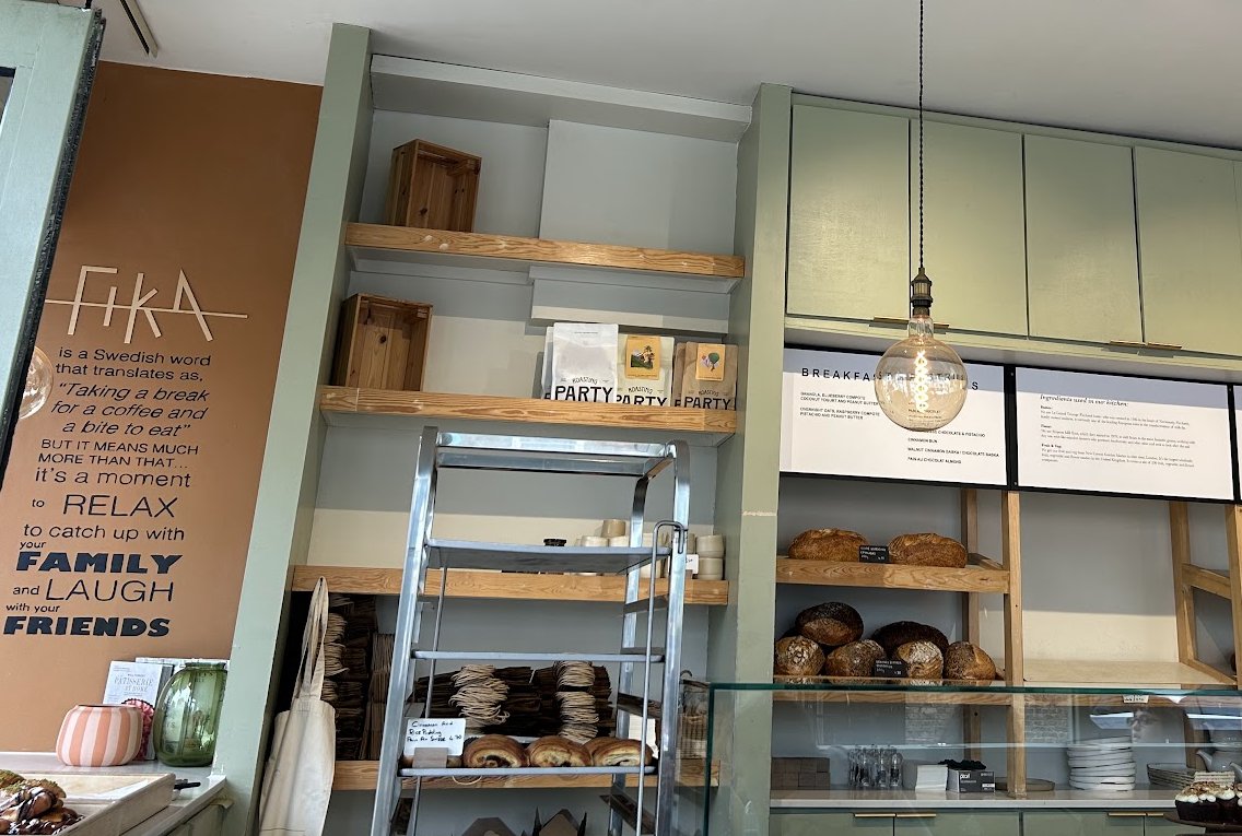 Inside Fika: the painted FIKA wall, sage-green shelves stacked with sourdough loaves and the breakfast menu board