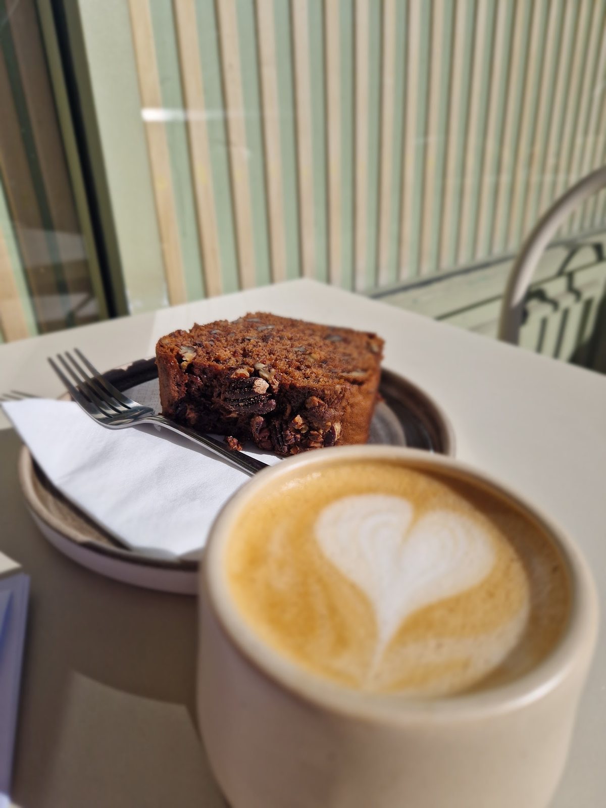 A flat white with latte-art and a slice of carrot and walnut cake in the sun at Fika, Lower Clapton