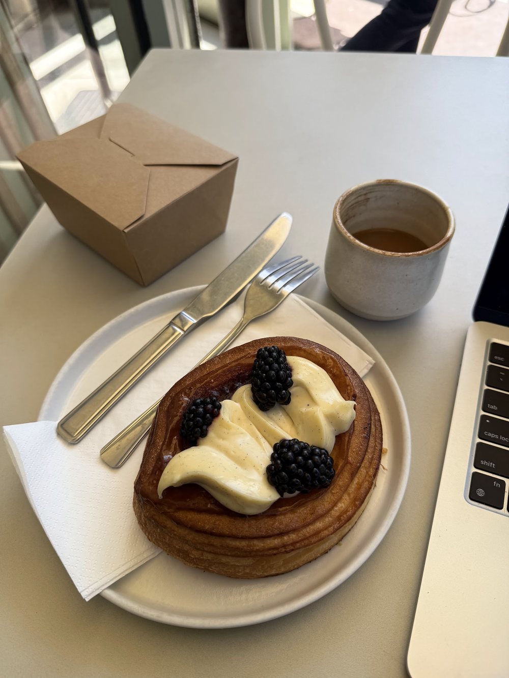 A pastry topped with vanilla cream and blackberries beside a coffee at Fika